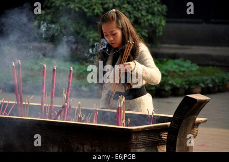 XINDU, CINA: giovane donna pone tre bruciare bastoncini di incenso in un braciere a Bao Guang Tempio (dinastia Qing) Foto Stock