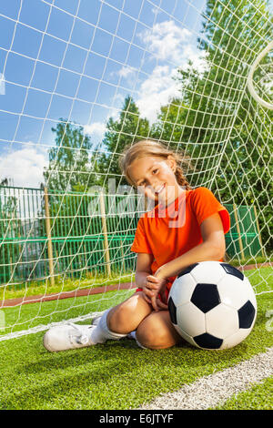 Ragazza con il braccio sul calcio si siede vicino a oggetti in legno Foto Stock