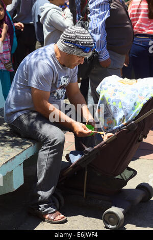 L'uomo alimentazione di un bambino in un passeggino in Banos, Ecuador Foto Stock