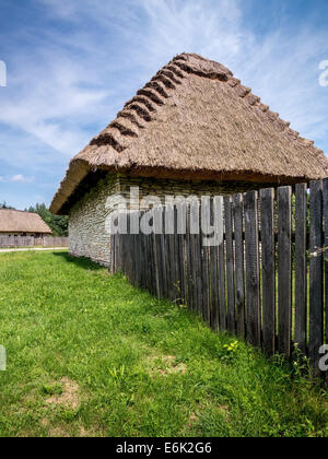 Cascina con cottage con tetto in paglia e Picket Fence shot contro il cielo blu Foto Stock