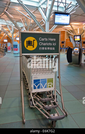 Bagagli o carrelli per bagagli del terminal dell'Aeroporto di Vancouver (YVR) in Canada. Sign in tre lingue. I chioschi di check-in. Foto Stock