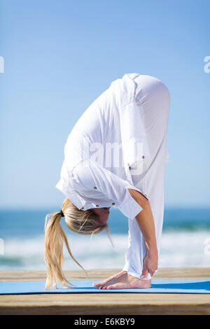 Donna di mezza età in bianco fare yoga sulla spiaggia Foto Stock