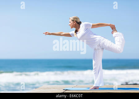 Montare la donna di mezza età in bianco facendo esercizi yoga in spiaggia Foto Stock
