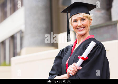 Felice donna di mezza età con graduazione cappello e camice azienda diploma Foto Stock
