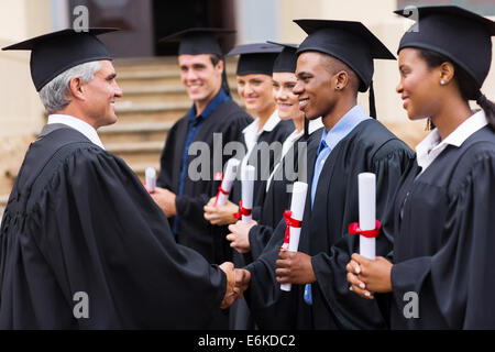 Senior professore universitario lo handshaking con giovani laureati Foto Stock