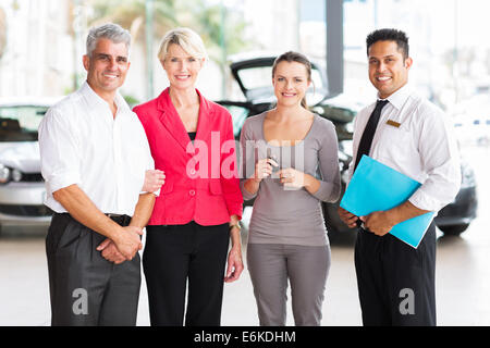 Famiglia di tre piedi con venditore presso la concessionaria del veicolo dopo l'acquisto di una nuova auto Foto Stock