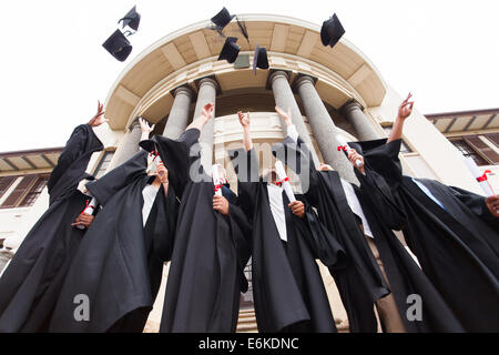 Gruppo di felice laureati gettando la laurea cappelli in aria per celebrare Foto Stock