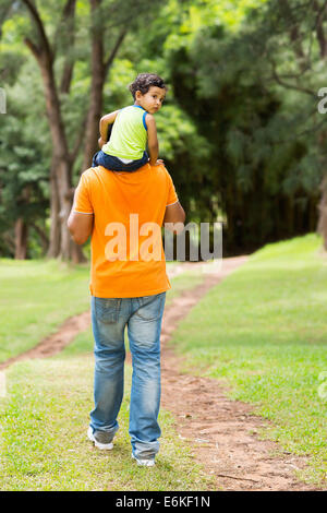 Carino piccolo ragazzo seduto sul padre di spalle all'aperto Foto Stock
