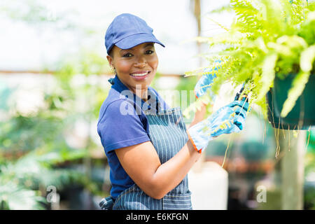 Sorridente americano africano giardiniere femmina la potatura di una pianta in serra Foto Stock