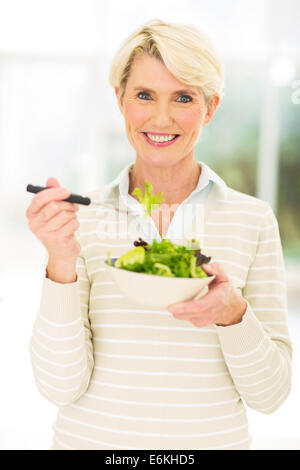 Felice donna di mezza età di mangiare insalata verde Foto Stock