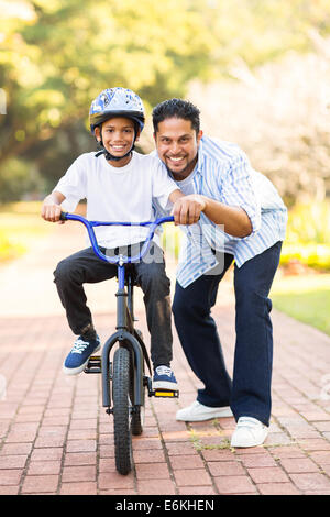 Happy little indian boy imparare ad andare in bicicletta con aiuto di suo padre Foto Stock