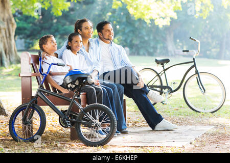 Moderna famiglia indiana seduta sul banco di lavoro e rilassarsi nel parco Foto Stock