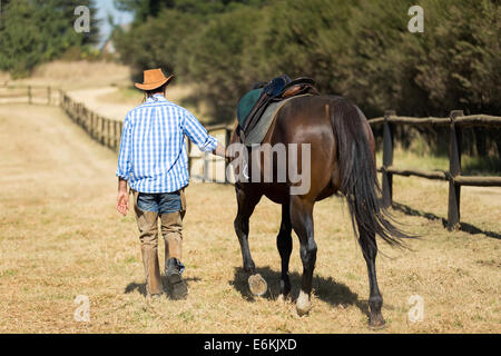 Vista posteriore del cowboy camminando con il suo cavallo Foto Stock