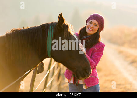 Attraente giovane donna in piedi accanto a un cavallo al mattino Foto Stock