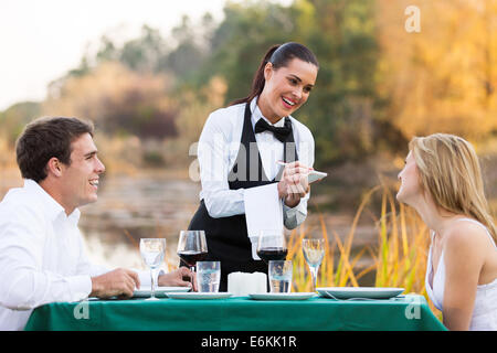 Amichevole cameriera femmina facendo ordine da carino coppia giovane Foto Stock