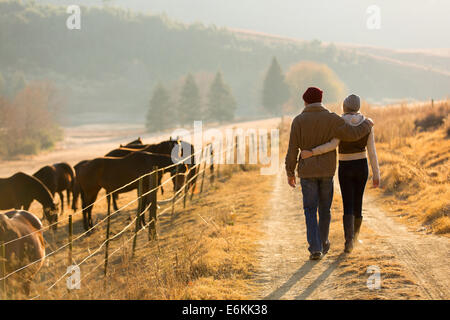 Vista posteriore della coppia giovane a piedi nella farm road Foto Stock