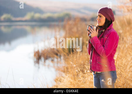 Giovane donna tenendo calda tazza di caffè in piedi vicino al lago Foto Stock