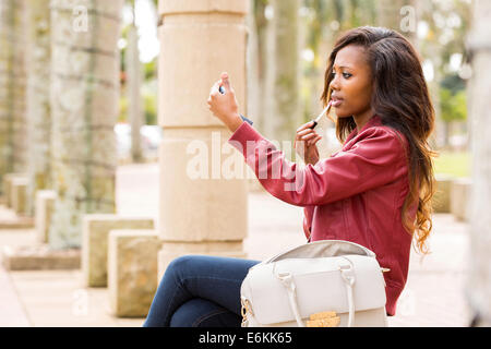 Bella donna africana specchio di contenimento e applicando lip gloss Foto Stock
