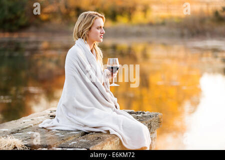 Premurosa donna con un bicchiere di vino rosso seduto sul molo Foto Stock