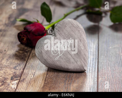 Il giorno di San Valentino il simbolo. Cuore su uno sfondo di legno con una rosa rossa. Foto Stock