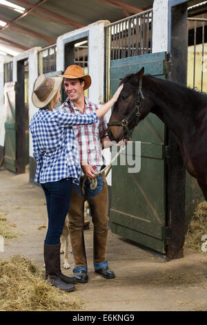 Felice cowboy e cowgirl giovane dentro stalle con il loro cavallo Foto Stock