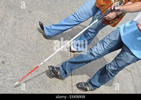 Cieco con un cieco di bastone da passeggio e una donna su una strada Foto Stock