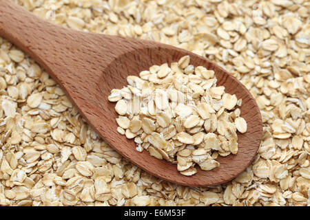 Fiocchi d'avena (fiocchi di avena) in un cucchiaio di legno su una di fiocchi d'avena sfondo. Primo piano. Foto Stock