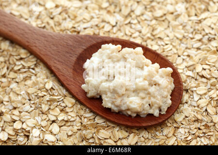 Porridge in un cucchiaio di legno su una di fiocchi d'avena sfondo. Primo piano. Foto Stock