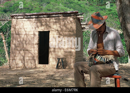 Uomo che fa un tradizionale cappello di paglia. Egli appartiene alla tribù Wayuu. Sullo sfondo di una capanna di fango ( Colombia) Foto Stock
