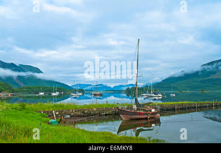 Vecchia barca in legno per la vendita Ormeggiata al pontile abbandonati su Loch Leven, Glencoe, tranquilla mattinata estiva, di nebbia in aumento, Highlands, Scozia Foto Stock