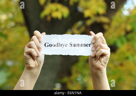 Frammenti di carta con le parole dicendo 'addio estate' nella donna le mani contro lo sfondo di autunno. Foto Stock