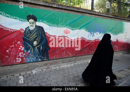 Velata donna iraniana, passeggiate passato un ayatollah Khomeini di immagine dipinta su un muro della ex Ambasciata degli Stati Uniti a Tehran, Iran. Foto Stock