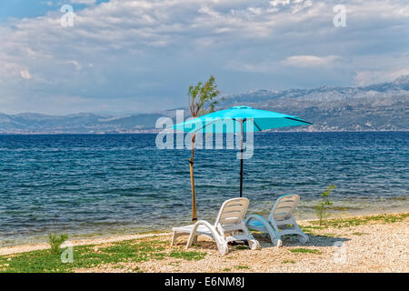 Due sedie a sdraio e ombrellone blu sulla spiaggia in riva al mare a Supetar sull'isola. Foto Stock