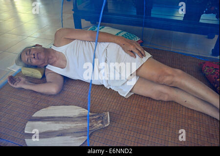 Senior Man (70) addormentato sul pavimento del soggiorno sotto una zanzariera, Hue, Vietnam, Sud-est asiatico Foto Stock