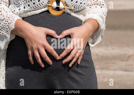 Donna incinta tenendo le sue mani sul suo ventre a forma di cuore Foto Stock