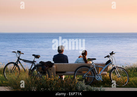 Due ciclisti riposo su una panchina a guardare il cielo di sera sul mare. Foto Stock