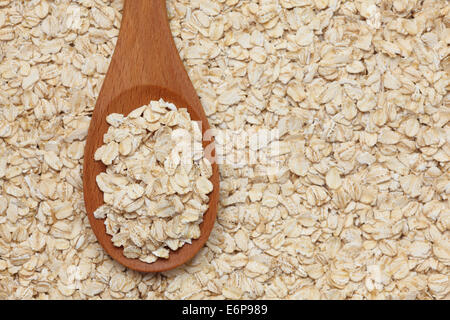 Fiocchi d'avena (fiocchi di avena) in un cucchiaio di legno su una di fiocchi d'avena sfondo. Foto Stock