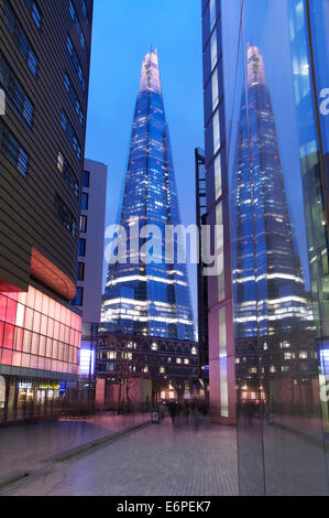 La Shard riflettendo nelle finestre dei moderni edifici per uffici di più luogo di Londra. Luci al neon brillare sul bagnato marciapiedi. Londra, Inghilterra, Regno Unito. Foto Stock