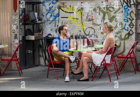Un bianco giovane condividendo un drink e parlare a un alfresco café tabella di Soho a New York City Foto Stock