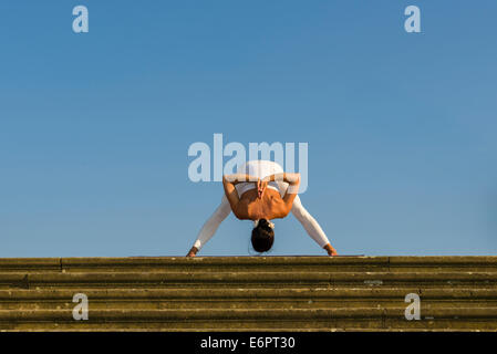 Giovane donna pratica di Hatha yoga, all'aperto, che mostra la posa Prasarita padottanasana, ampia zampe piegare in avanti Foto Stock