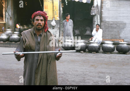 Povero uomo musulmano pregando davanti ad un mausoleo - moschea. Dietro di lui, cauldrons contenente cibo per i poveri ( Pakistan) Foto Stock