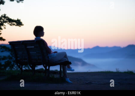 Giovane donna giapponese seduta su una panchina in campagna Foto Stock