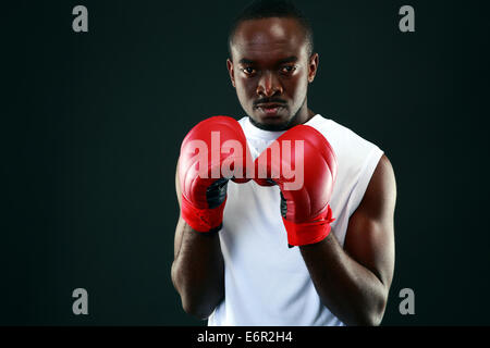 L'uomo africano nella boxe Guantoni boxe in piedi su sfondo nero Foto Stock