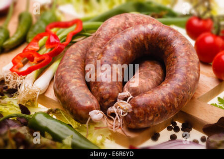 Salumi crudi con verdure su tavola di legno, fuoco selettivo Foto Stock