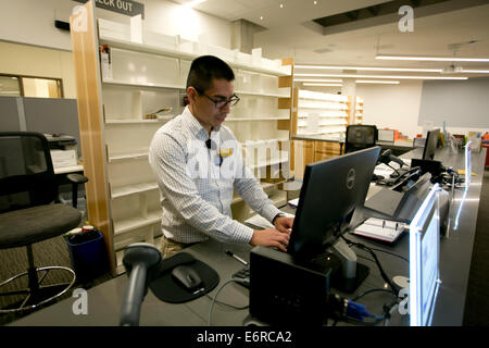 Ispanico bibliotecario maschio controlla il computer all'interno della biblioteca del nuovo Austin Community College edificio del campus di Austin in Texas Foto Stock