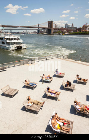 La gente a prendere il sole accanto a East River, Ponte di Brooklyn e South Street Seaport, Manhattan, New York, New York, Stati Uniti d'America Foto Stock