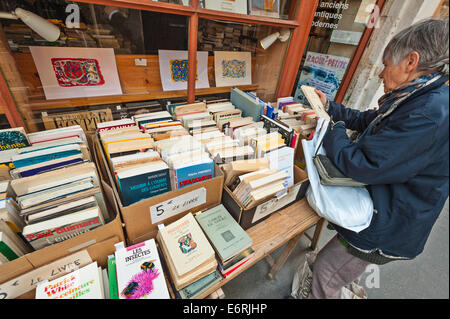 Una donna francese navigando attraverso le scatole di libri sul display in strada al di fuori di un libraio shop in Rousillon, Francia Foto Stock