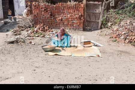 Local donna seduta sul ciglio della strada, lavorando setacciatura di grano, in un villaggio vicino a Deogarh, Rajasthan, India Foto Stock