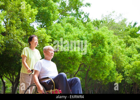 Asian senior uomo seduto su una sedia a rotelle con sua moglie Foto Stock