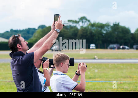 Fotografi provenienti da 3 diverse generazioni in piedi a fianco a fianco scattare fotografie con diverse attrezzature Foto Stock